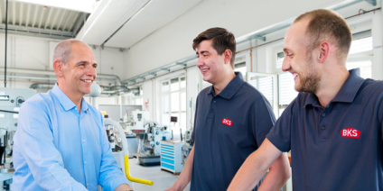 Profis in moderner Produktionshalle mit BKS-Logo Drei Männer im Gespräch in Werkstatt